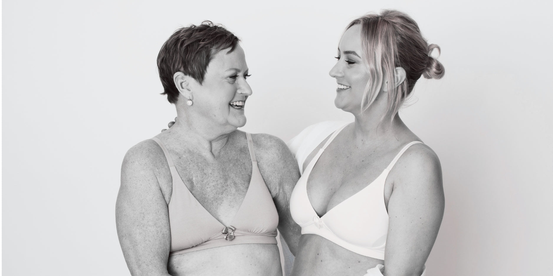 Two women laughing together wearing Anaono Molly Plunge Bra and Trish Molded Cup Plunge Bra in black and white photo