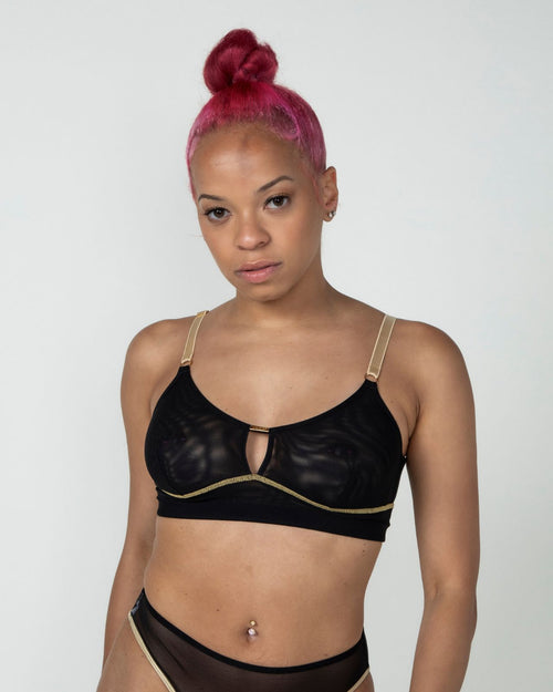 Black / Implants & model wearing the Victoria Pocketed Keyhole bralette with gold lace trim and gold jewel that says anaono