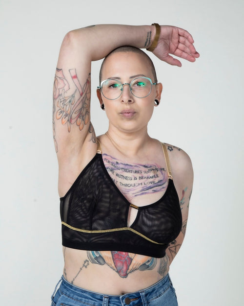 Black / Implants & model wearing the Victoria Pocketed Keyhole bralette with gold lace trim and gold jewel that says anaono