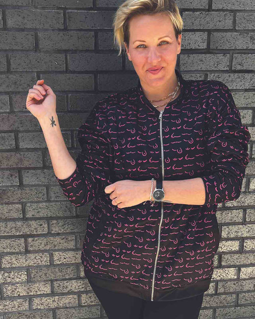 Black & pink boob printed bomber jacket with pockets and graphic boob prints on model up against a brick wall