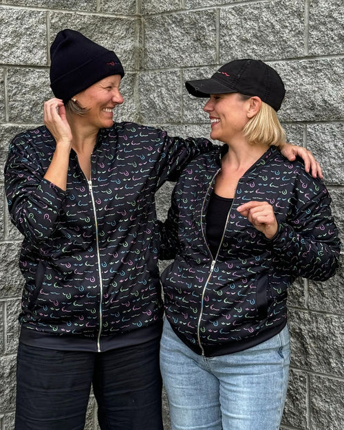 Black & group photo of two breast cancer survivors wearing the limited edition metastatic breast cancer awareness bomber jacket